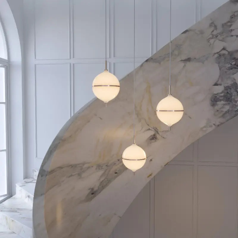 Three spherical pendant lights hanging in a modern interior setting with marble wall.