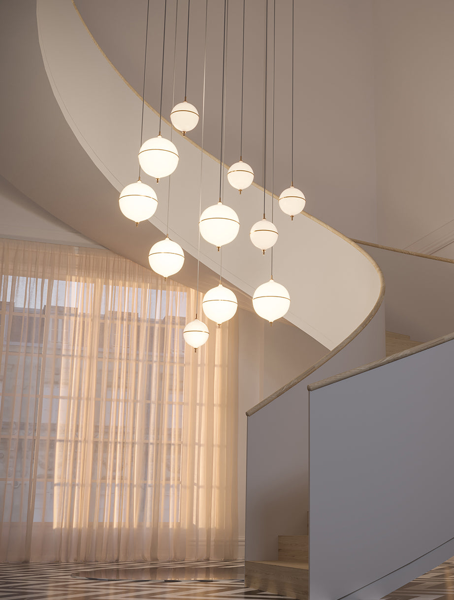 Pendant collection on a staircase. Features a sleek opal glass globe with brass detailing, offering warm ambient lighting and timeless sophistication for modern interiors.