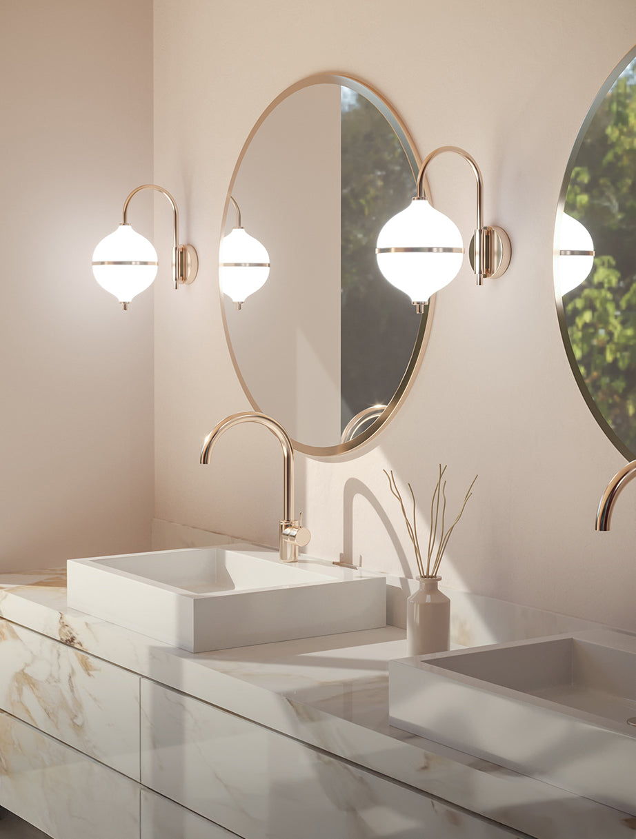 A wall lamp in a bathroom on both sides of the mirror. The design blends classic elegance with modern minimalism, featuring a curved brass-finished arm and a frosted opal glass globe for a refined, warm ambiance.