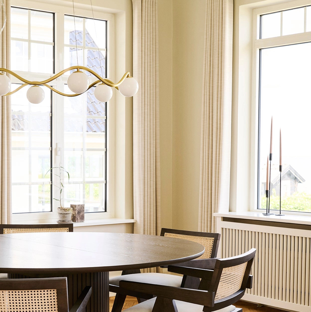 Dining room with a round wooden table and chairs near large windows.