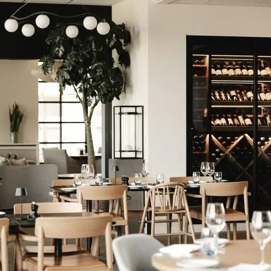 Modern restaurant interior with wooden chairs, tables, and a wine rack.