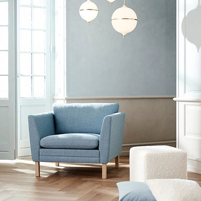Blue armchair in a modern living room with large windows and neutral walls.